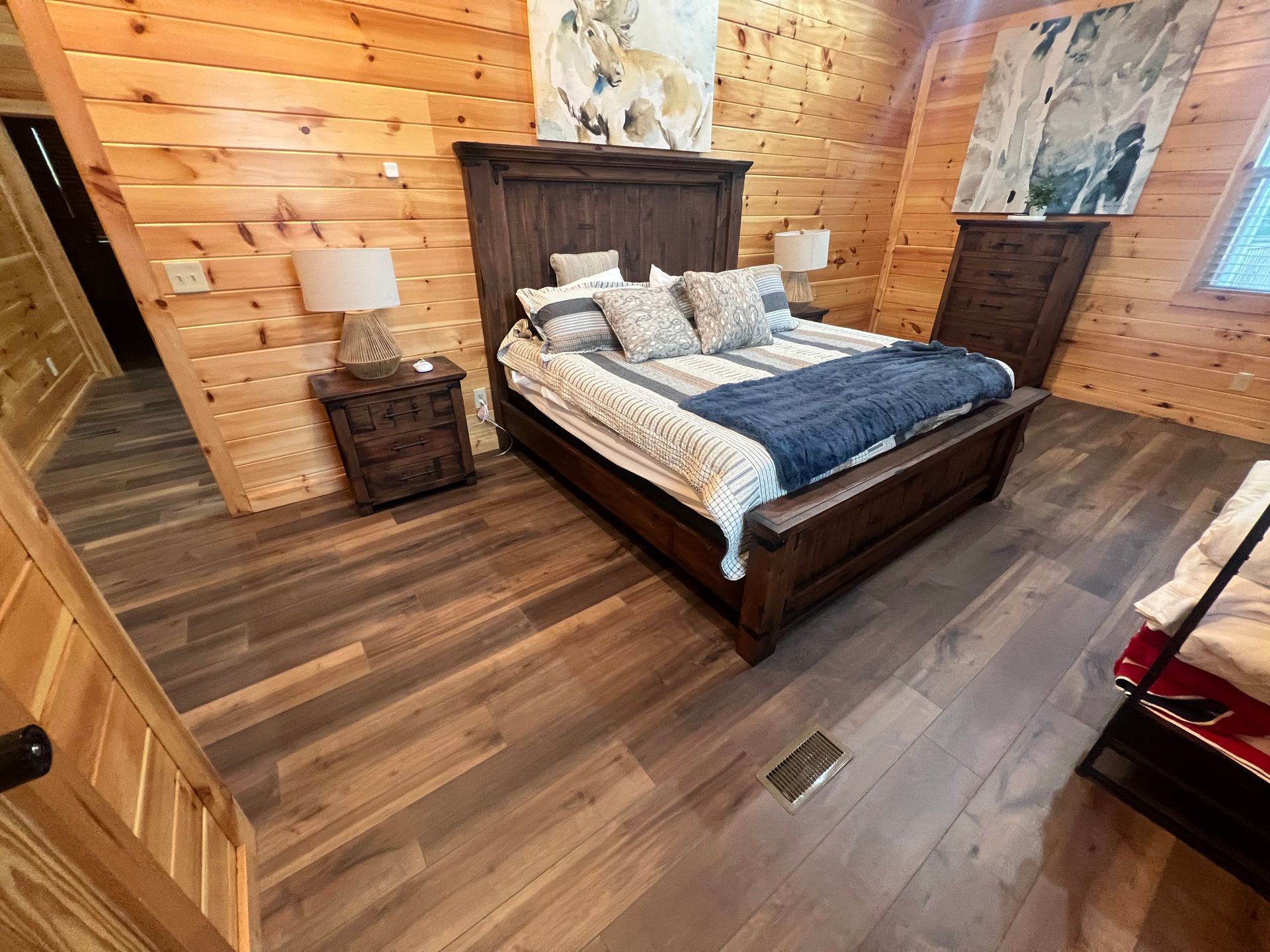 Rustic wood-paneled bedroom with a dark wood bed, blue-gray bedding, and bedside tables