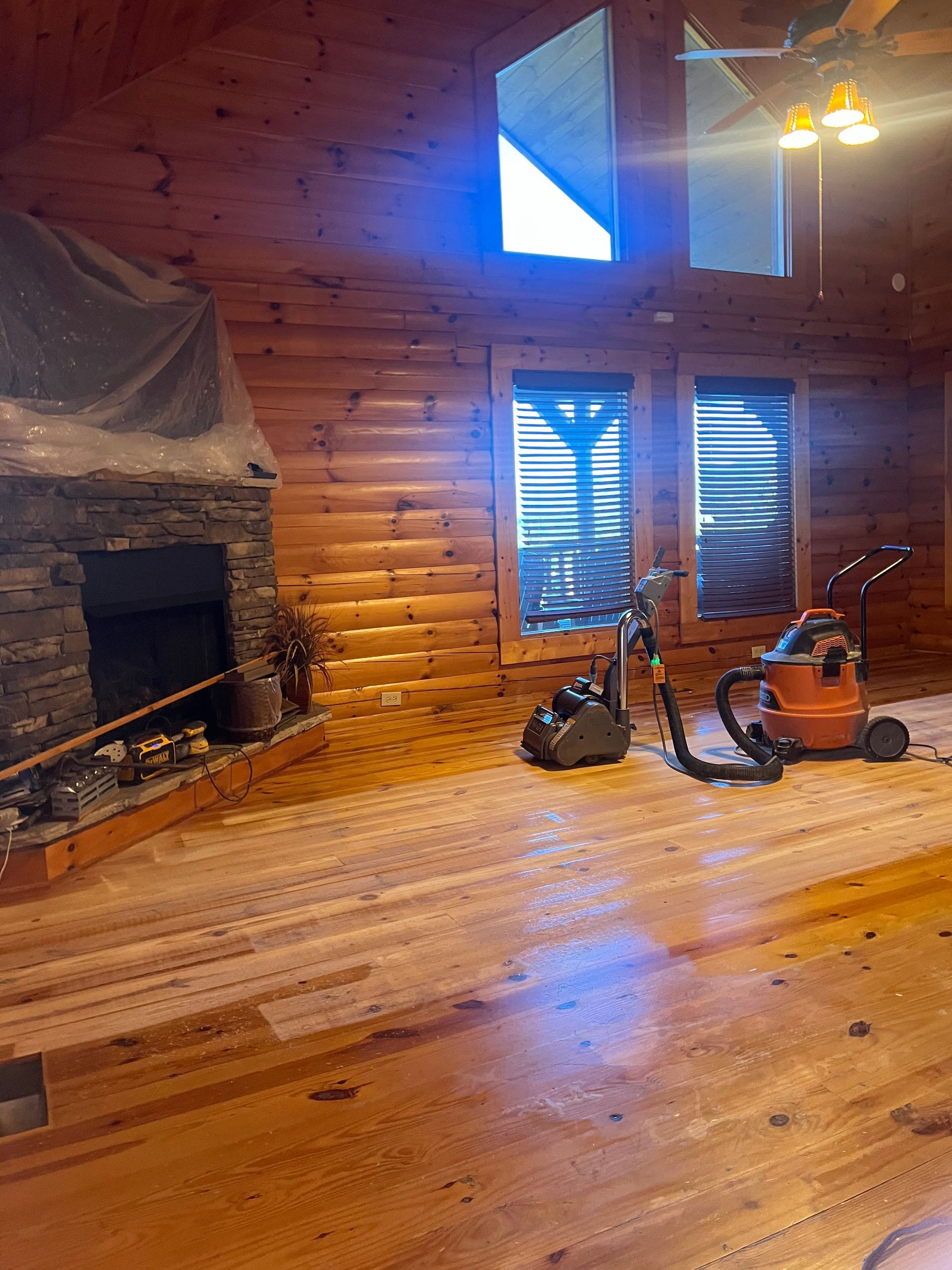 Rustic wood-paneled cabin interior with stone fireplace, bicycle, and orange power tool near windows
