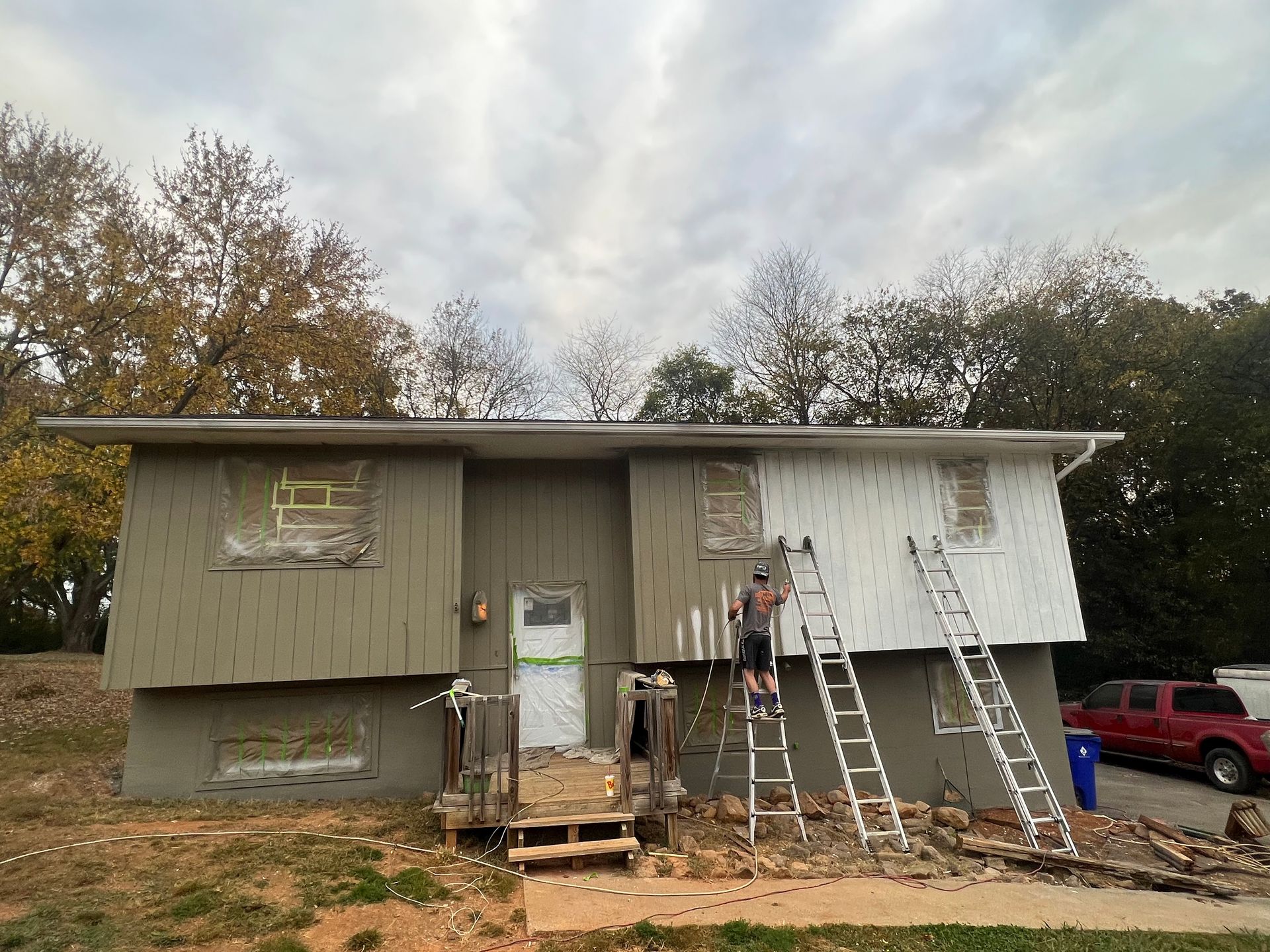 Two-story house under renovation with ladders, scaffolding, and workers on the front porch