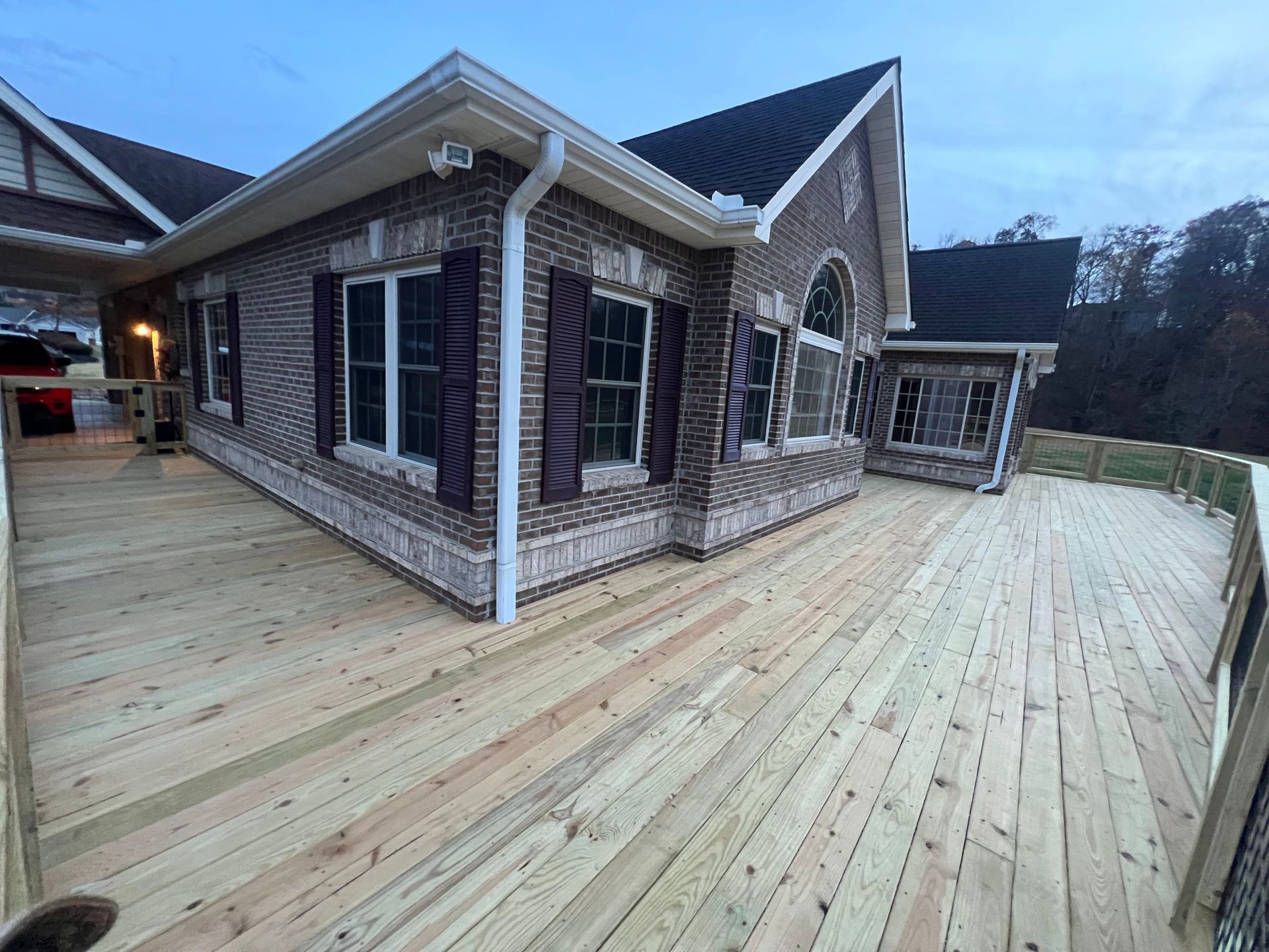 Brick house with a large wooden deck and white trim at dusk