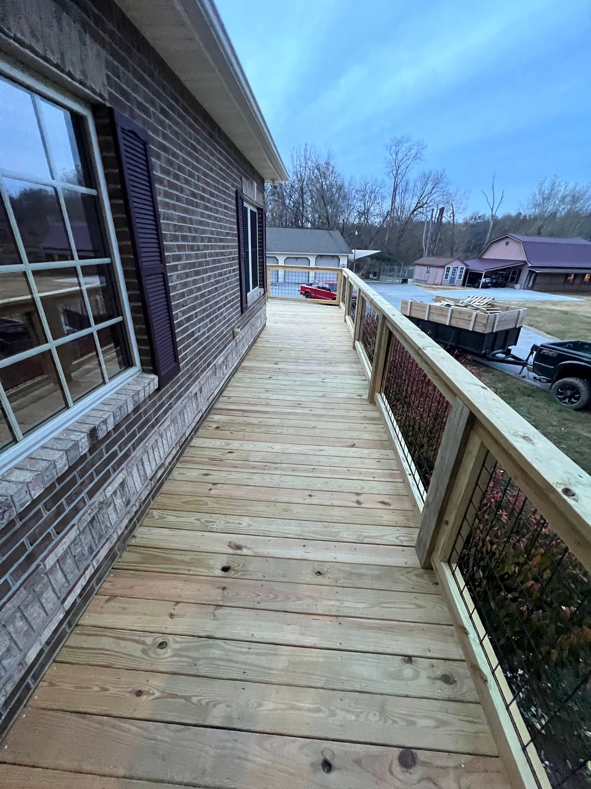 Wooden deck walkway along a brick house with white railing, overlooking a backyard at dusk