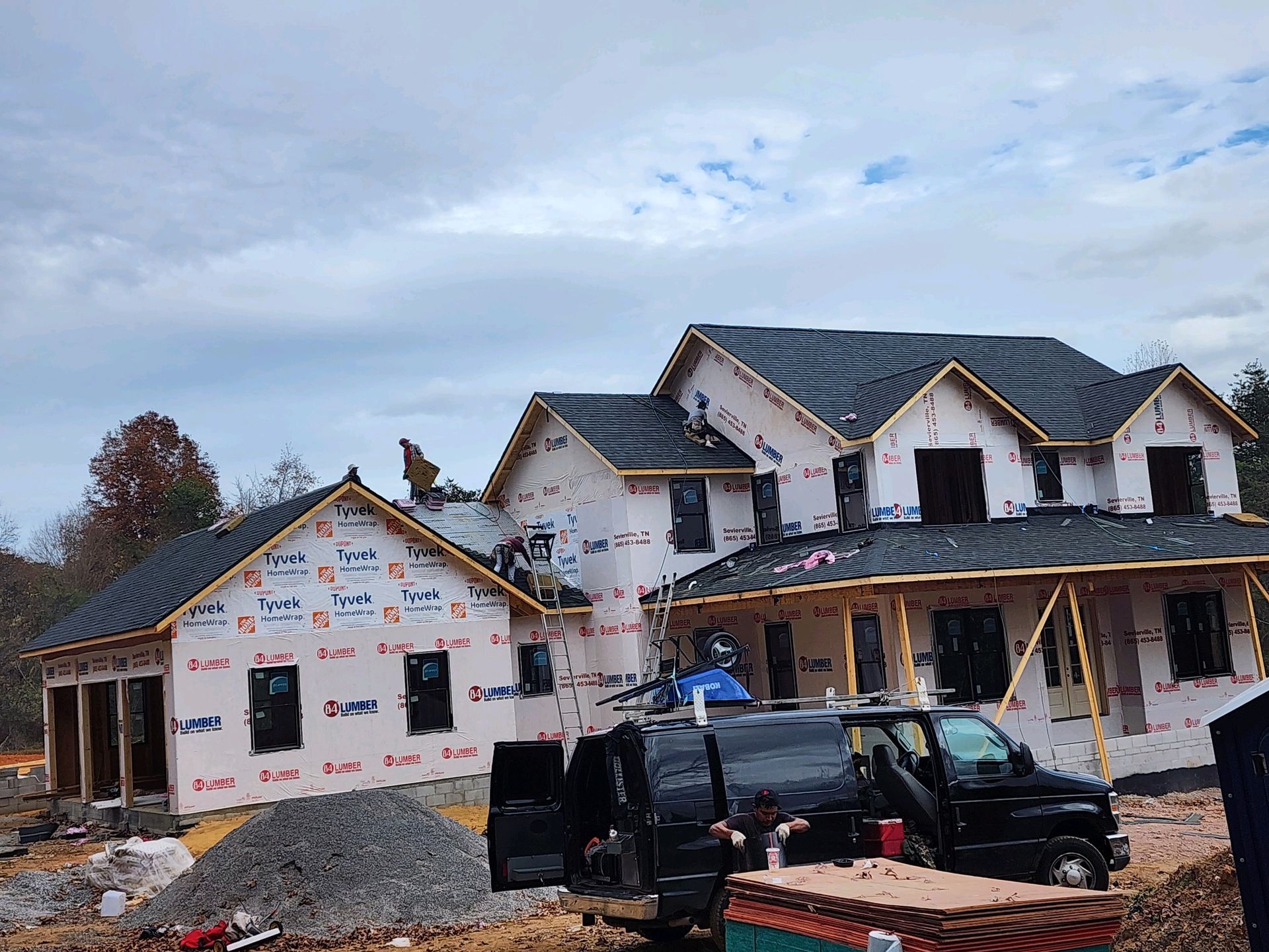 New house under construction with white siding, black roof, and construction materials in front