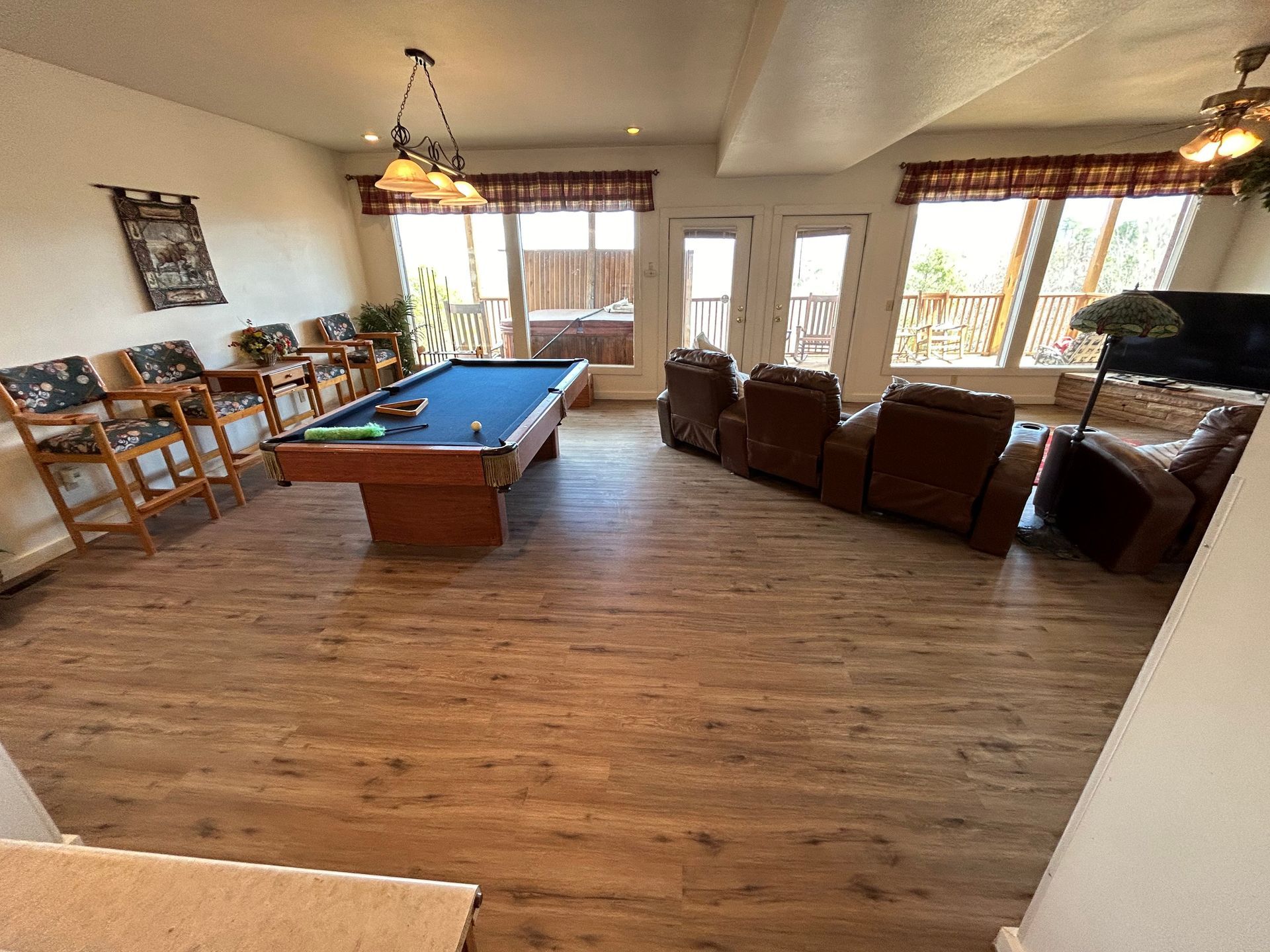 Spacious living room with a pool table, leather chairs, and large windows letting in daylight