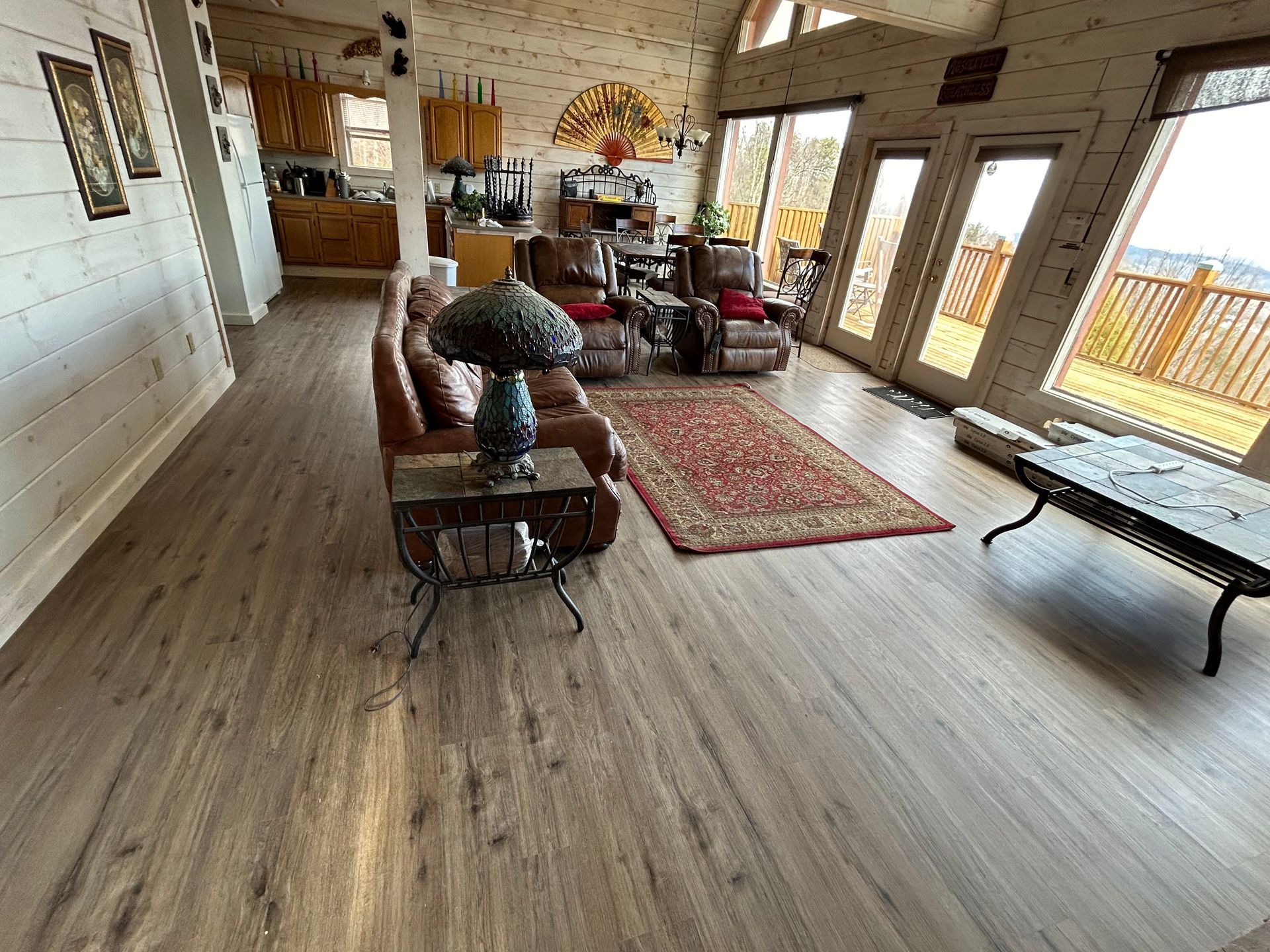 Spacious living room with leather sofa, wood floors, rugs, tall windows, and a billiards table.