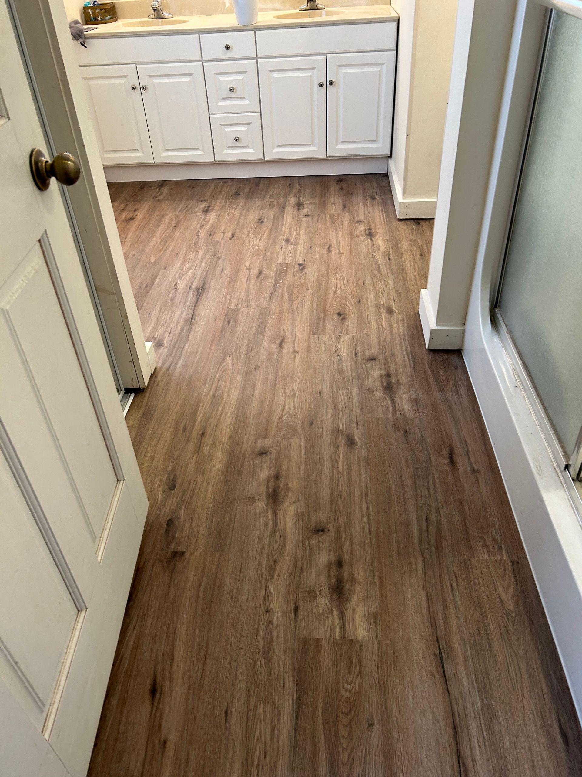 Narrow hallway with wood-look flooring leading to a white bathroom vanity and sink.