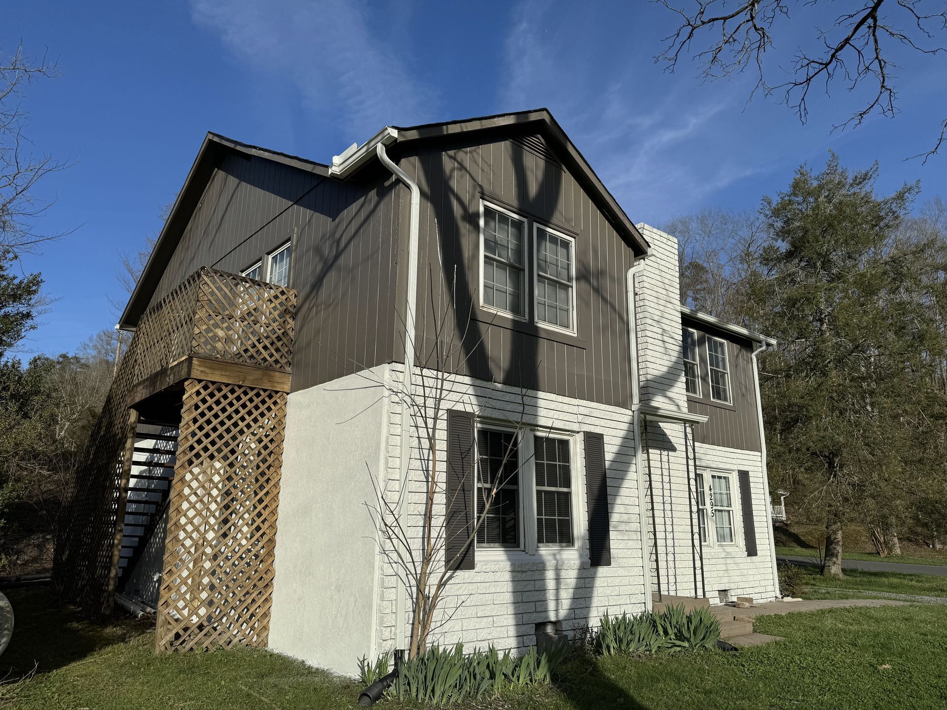 Two-story house with white and dark siding, a stone chimney, and exterior stairs on a grassy lot.