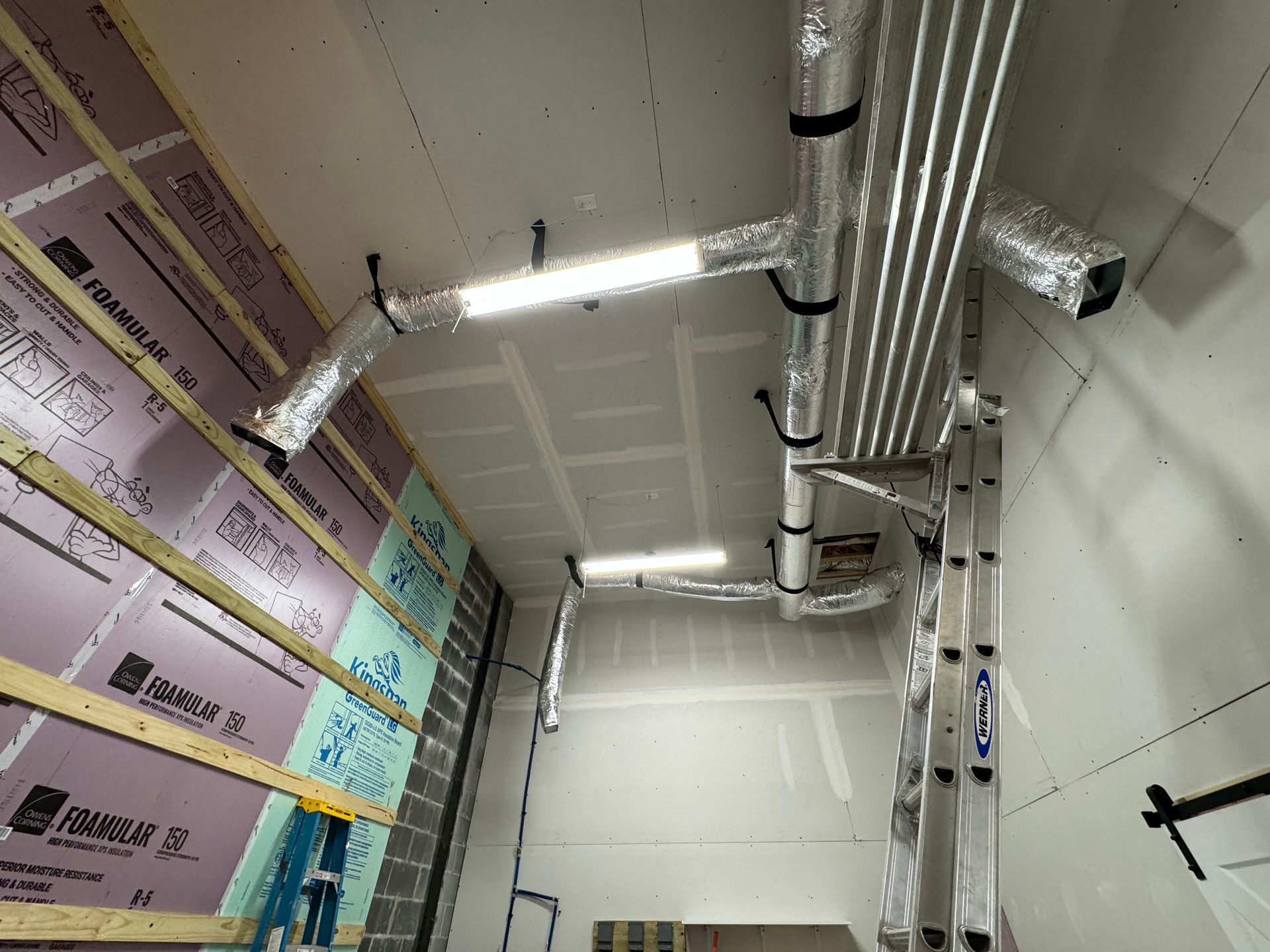 Interior of a building under construction with exposed ducts, pipes, insulation, and unfinished walls