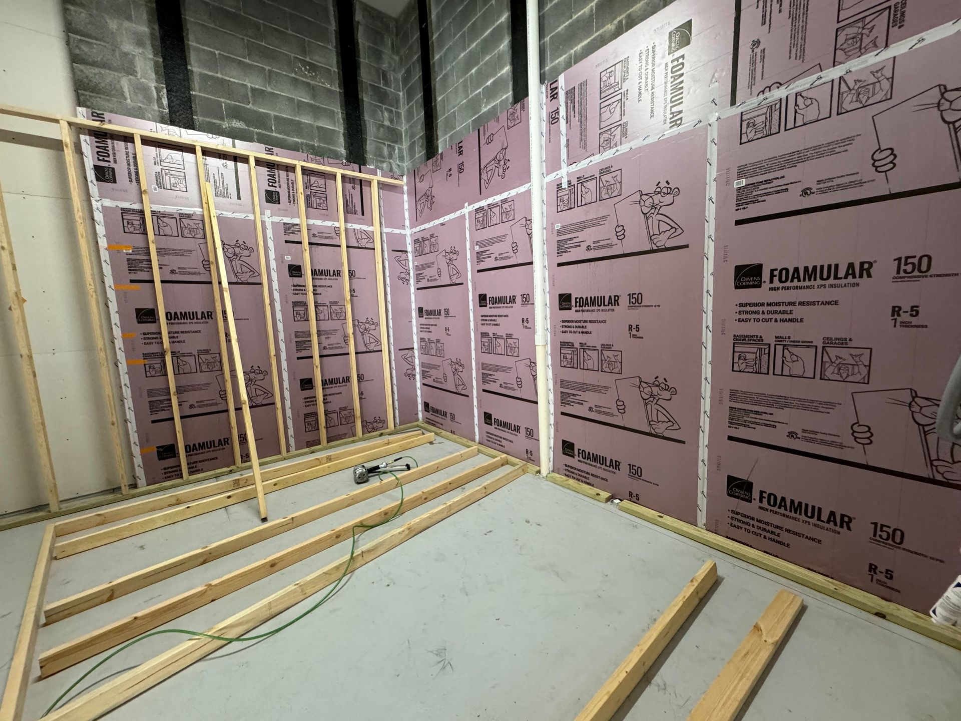 Unfinished basement framed with wood studs and pink insulation board on walls and floor.