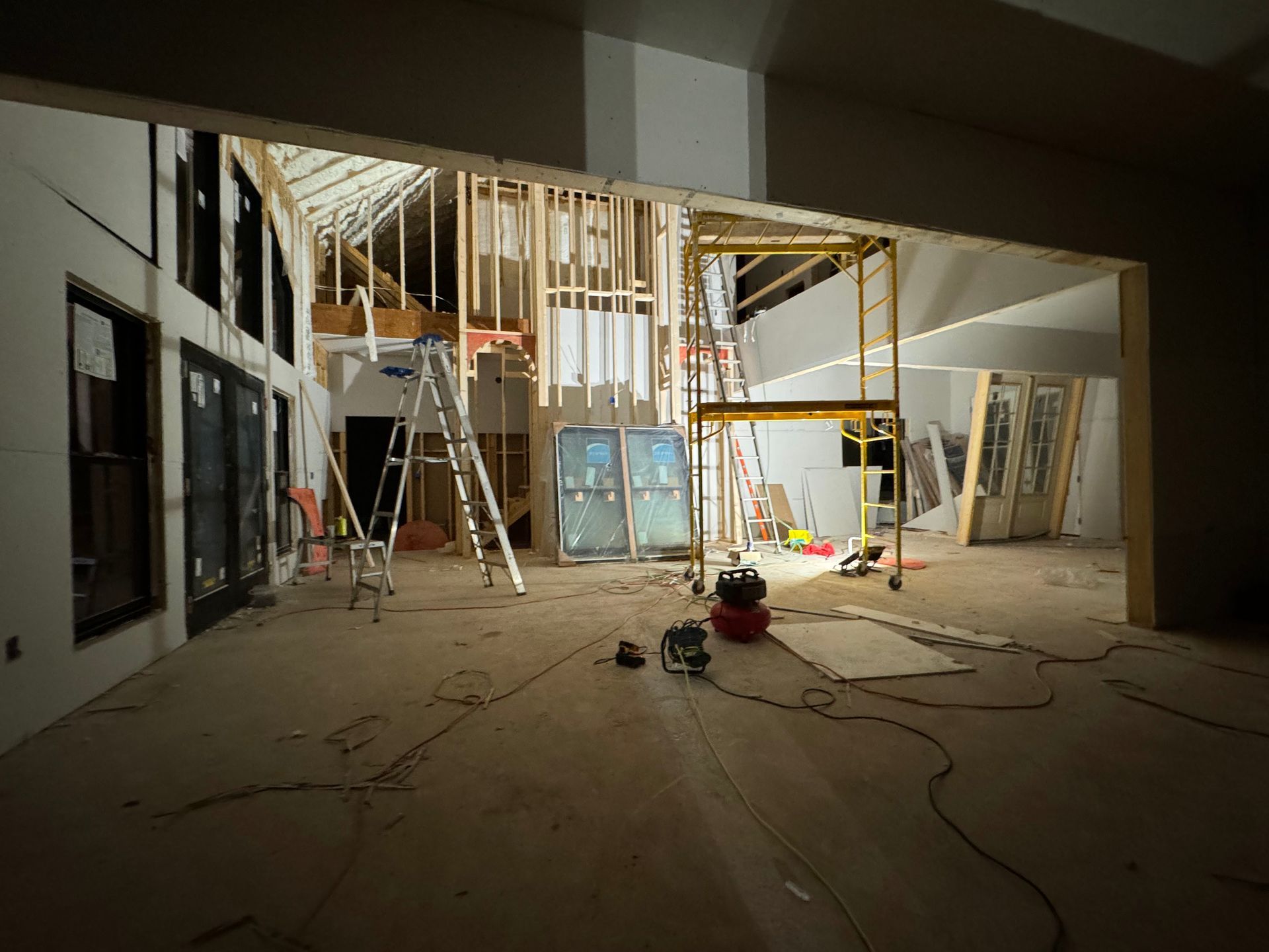 Interior construction site with ladders, exposed framing, and tools on a dusty floor