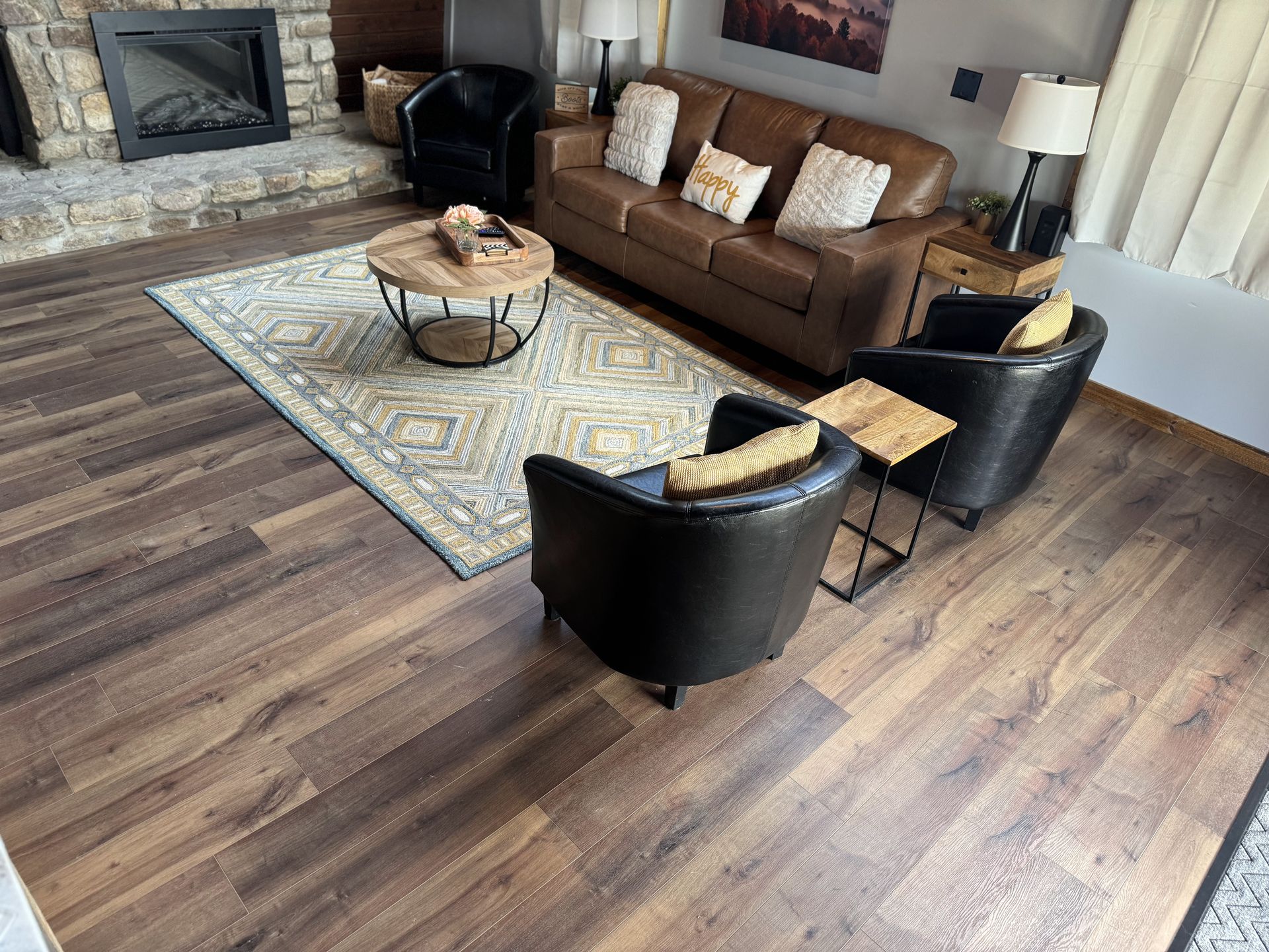 Modern living room with brown leather sofa, black chairs, stone fireplace, and patterned rug.