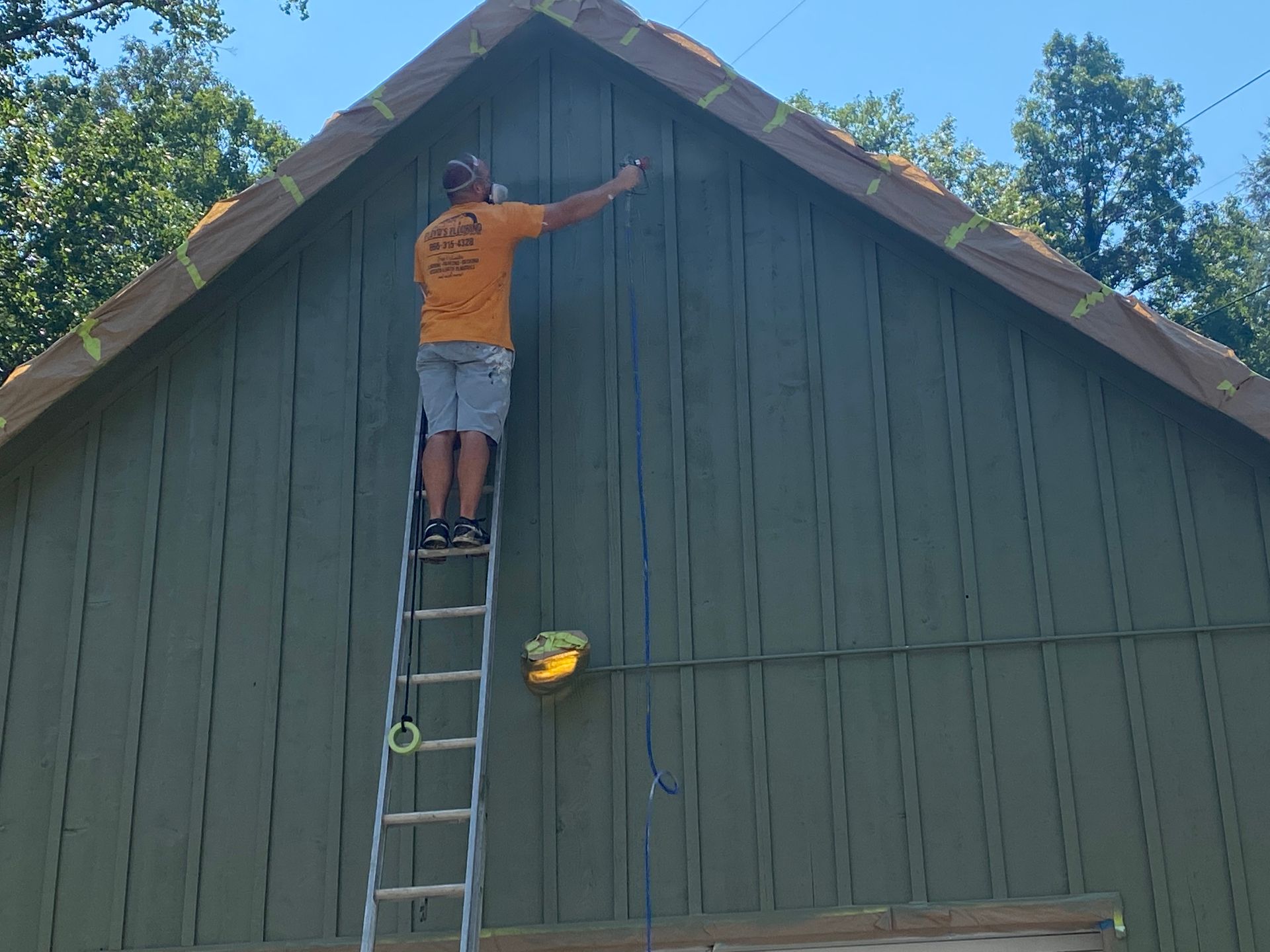 Person on a ladder painting the peak of a green house exterior