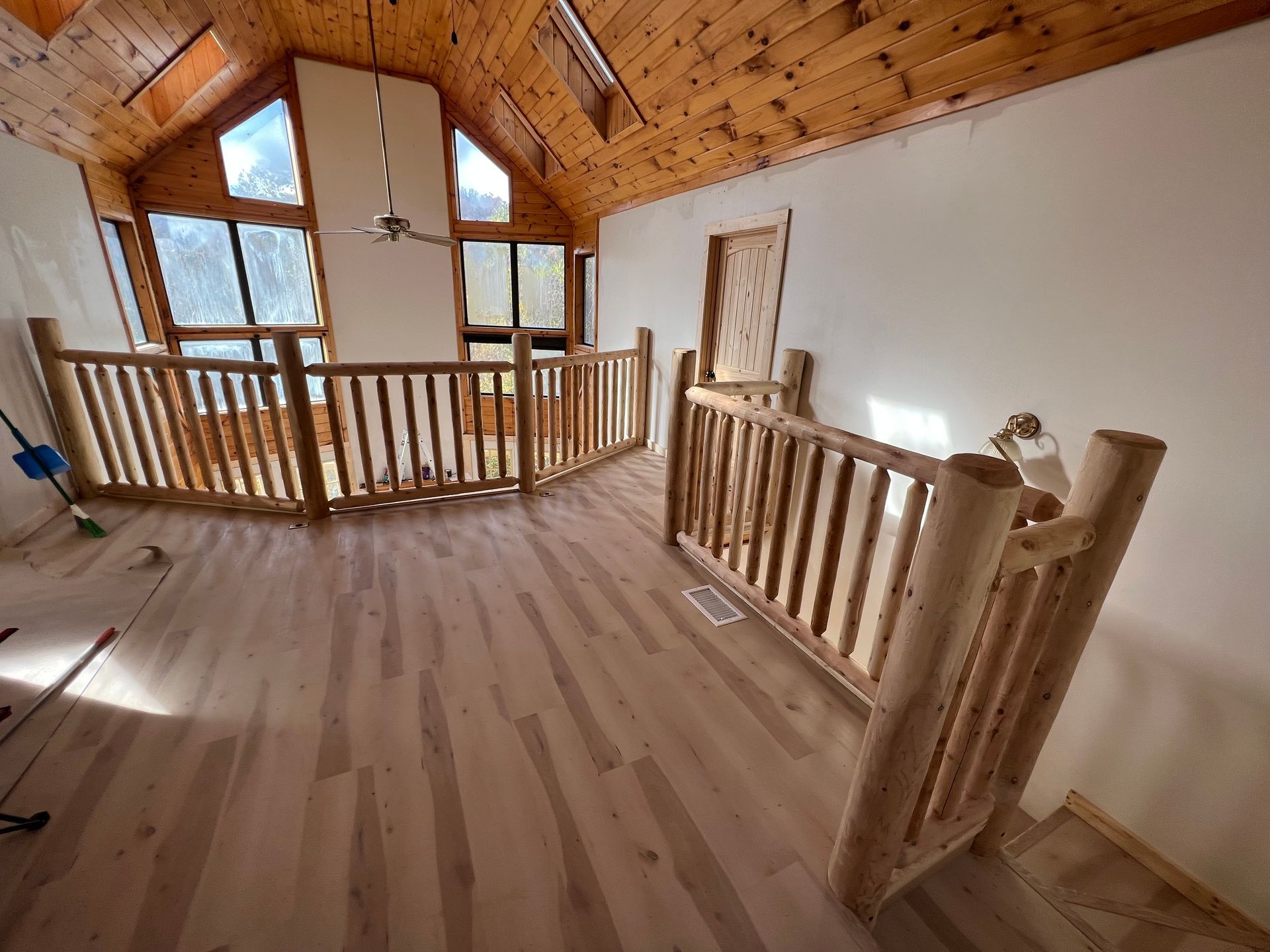 Empty loft with wood floor, vaulted ceiling, and a staircase railing overlooking a bright window.