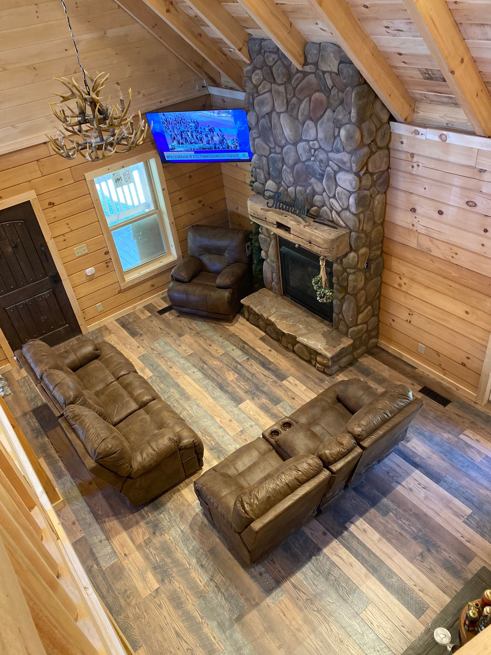 Cozy rustic cabin living room with leather sofas, stone fireplace, and wall-mounted TV