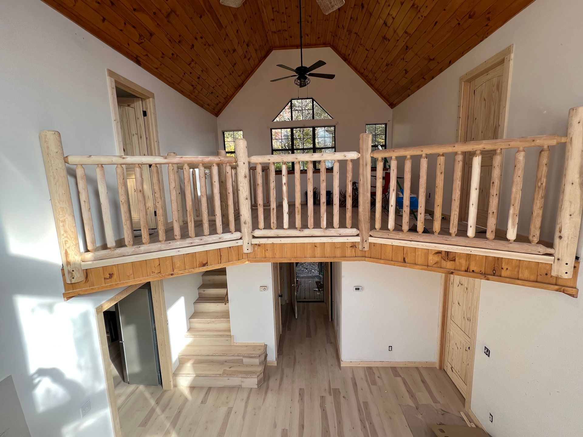 Loft interior with wooden balcony railing, vaulted wood ceiling, and open staircase below