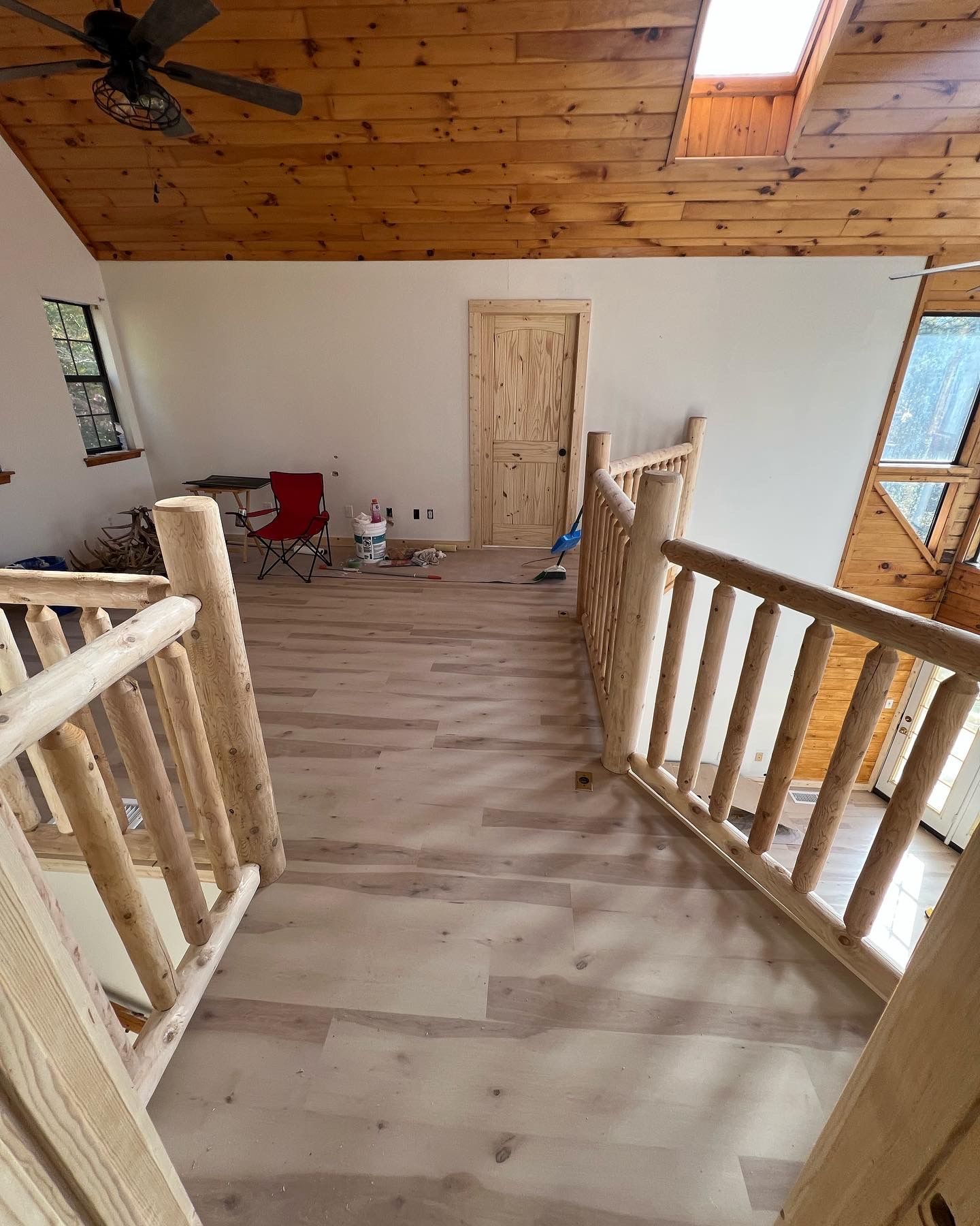 Wood-paneled loft with light flooring, unfinished walls, stairs, and a wooden door at the far end.