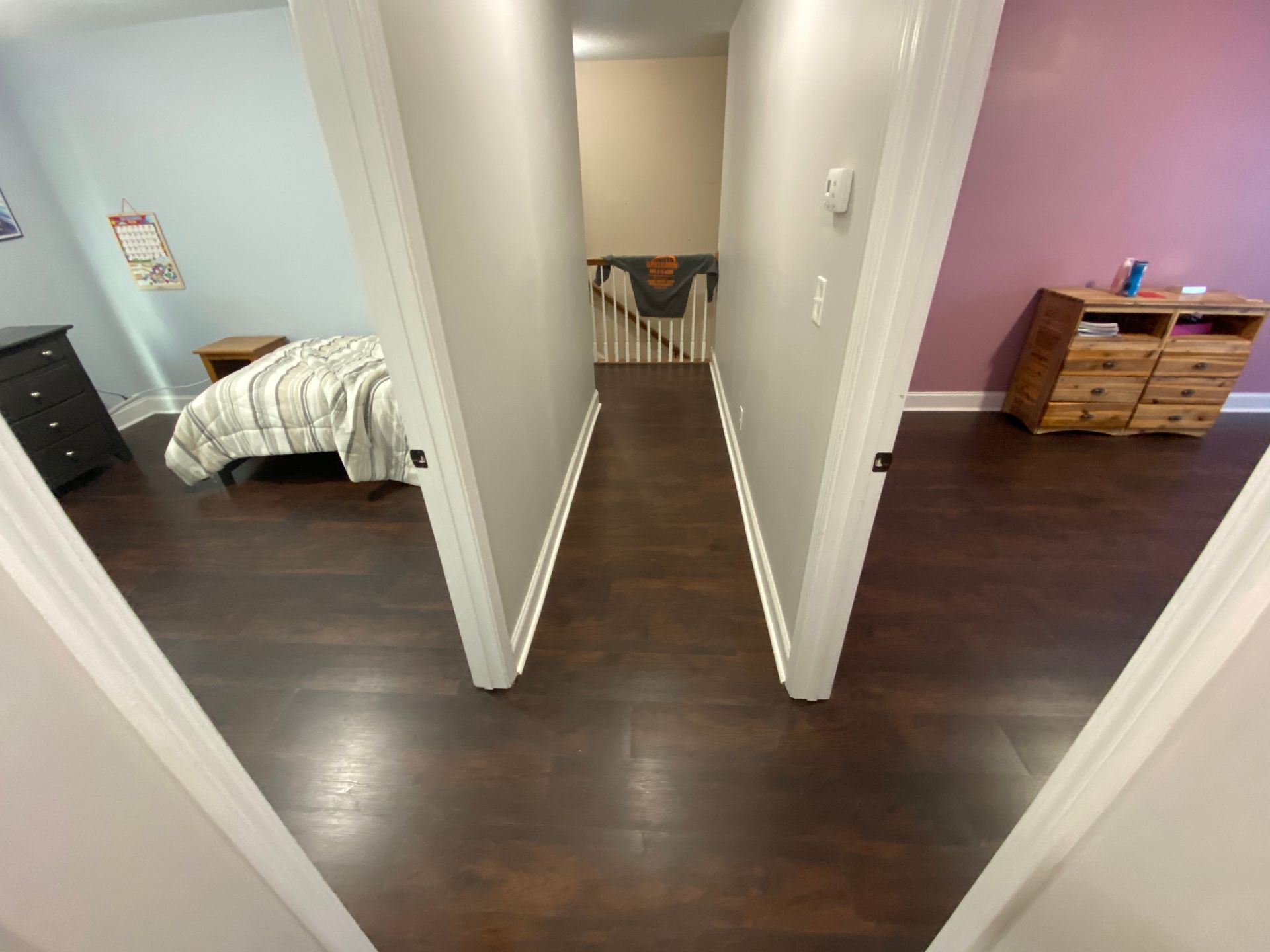 Hallway with dark wood floors, bedrooms on both sides, and a dresser at the end.