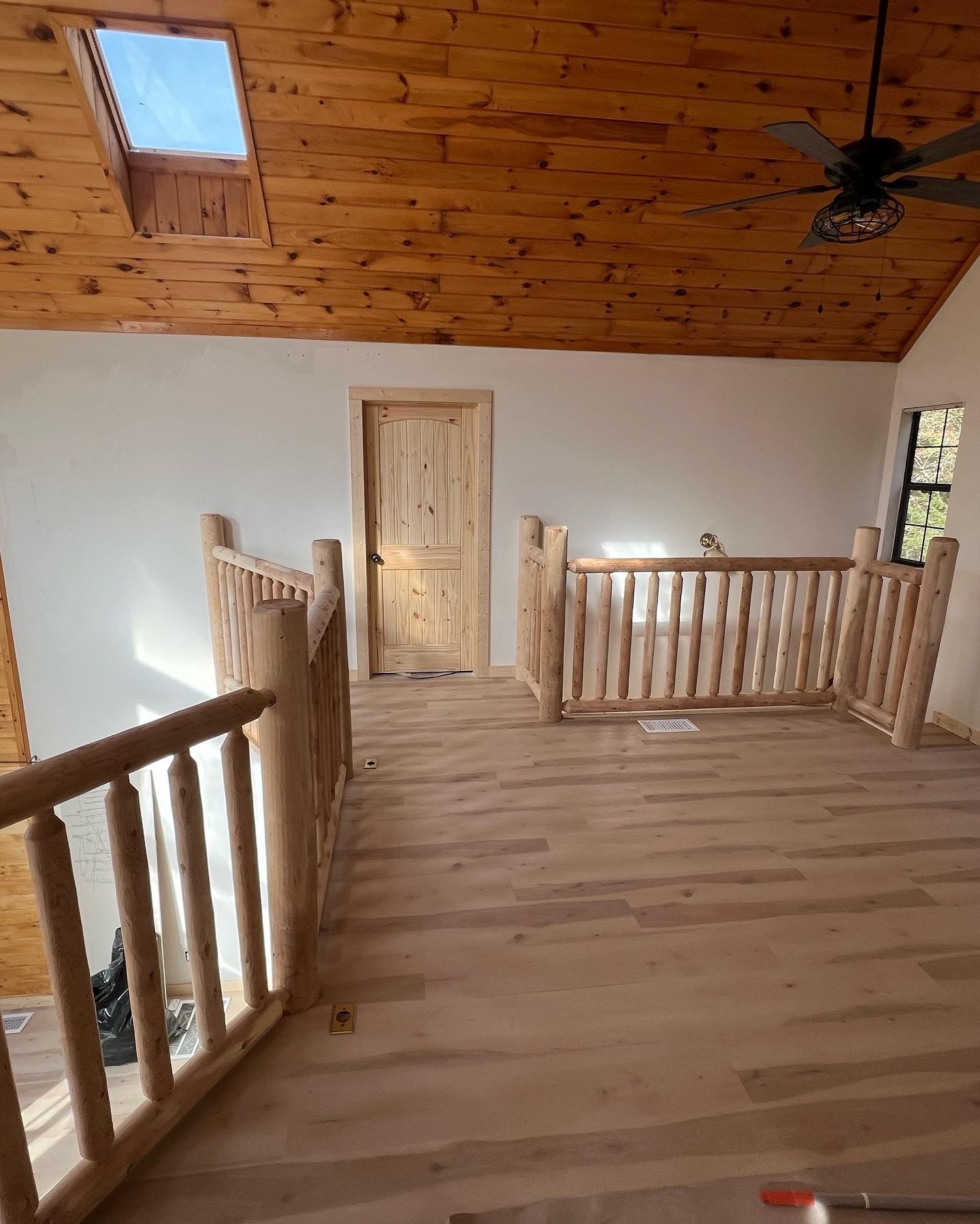 Wooden loft hallway with railing, central door, sloped wood ceiling, and skylight.