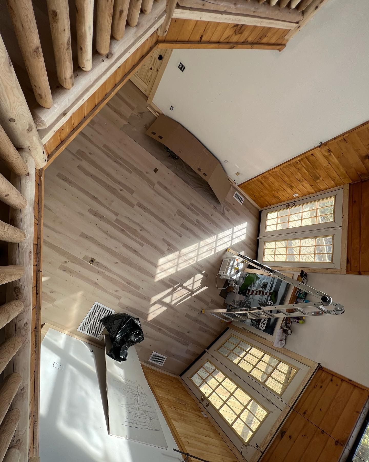 A bright room with wooden walls, large windows, and a workbench covered in tools and supplies.