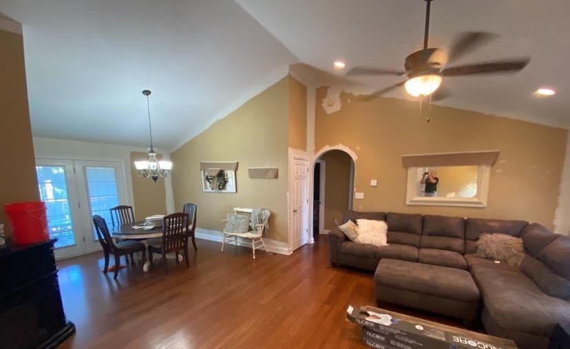 Open living and dining room with hardwood floors, brown sectional sofa, ceiling fan, and dining table by the window.