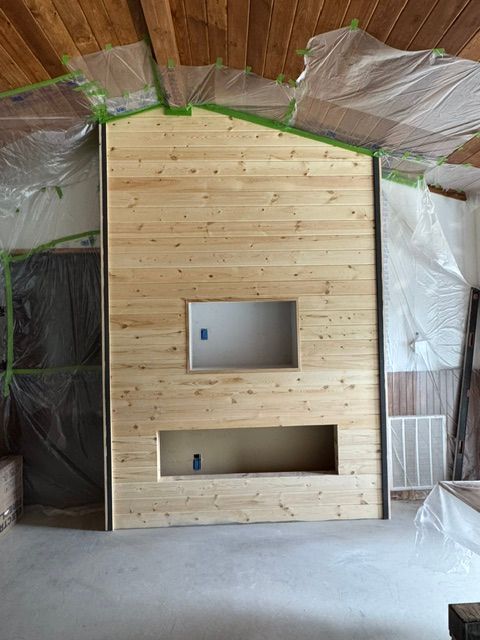 Wood-paneled wall with two rectangular cutouts in a construction space, partially covered with plastic sheeting.