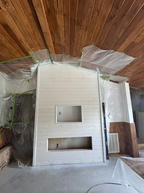 Renovation site with a white fireplace wall and two built-in openings under a wood-paneled ceiling