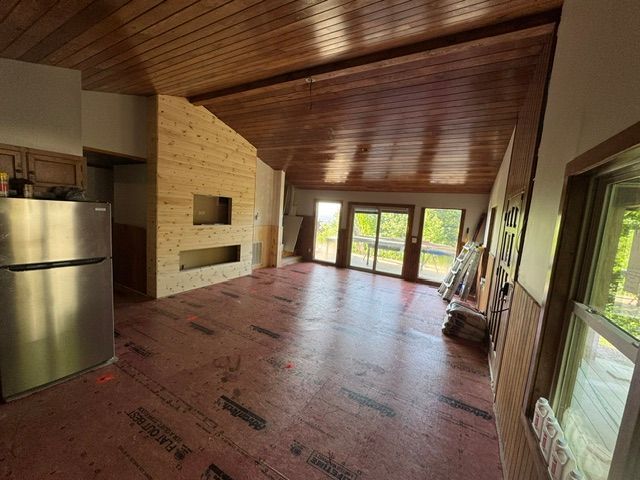 Empty room with wood ceiling, exposed insulation wall, stainless fridge, and glass doors to a deck