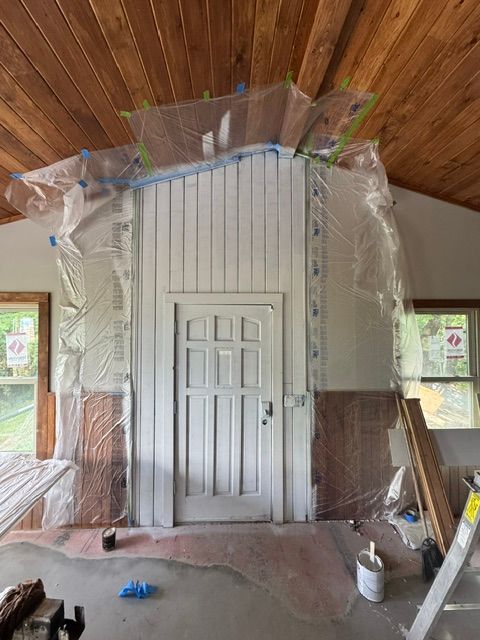 Plastic sheeting covers a tall white doorway in a wood-paneled room under renovation.