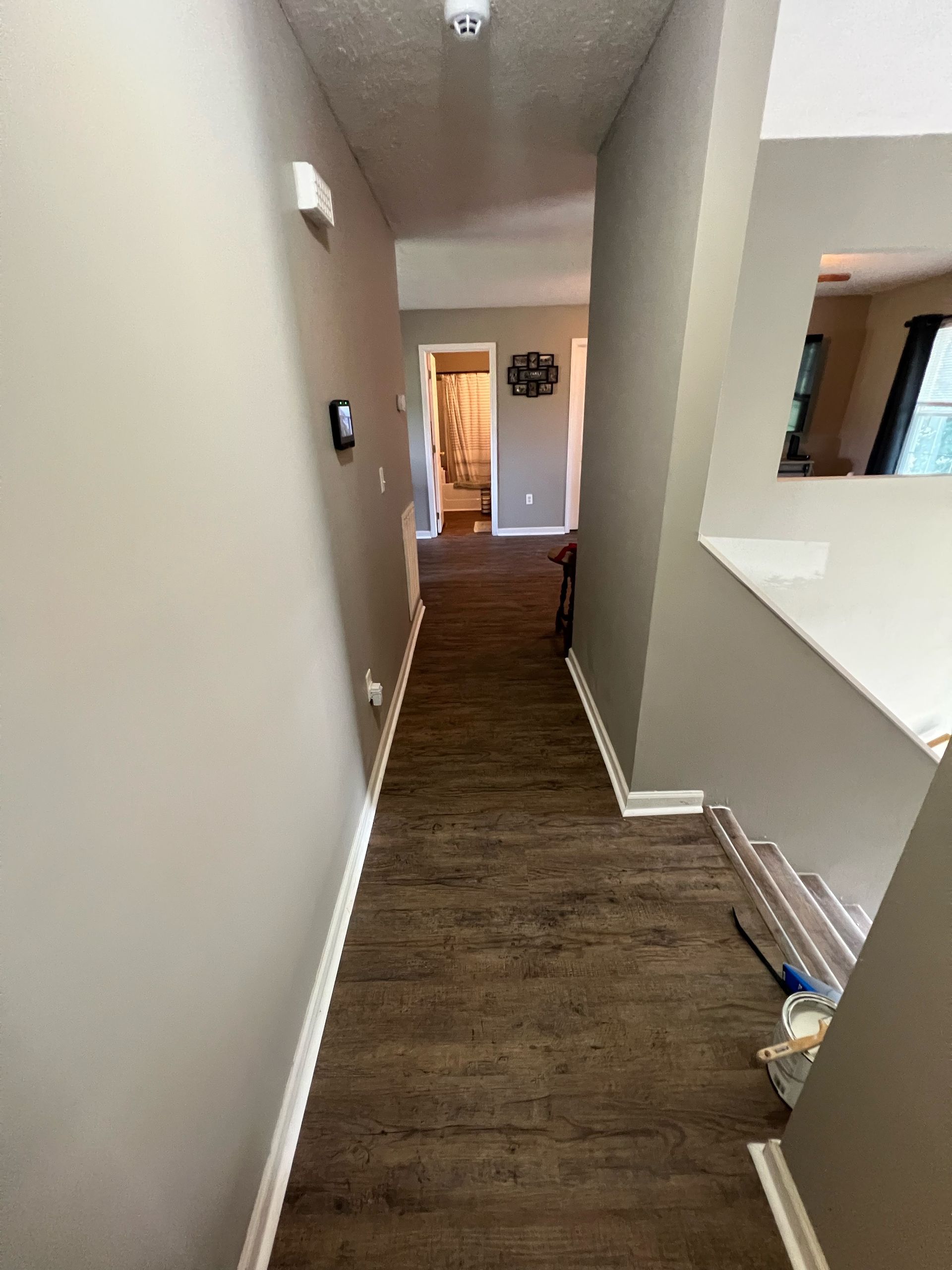 Narrow hallway with wood floor and gray walls leading to a bright doorway.
