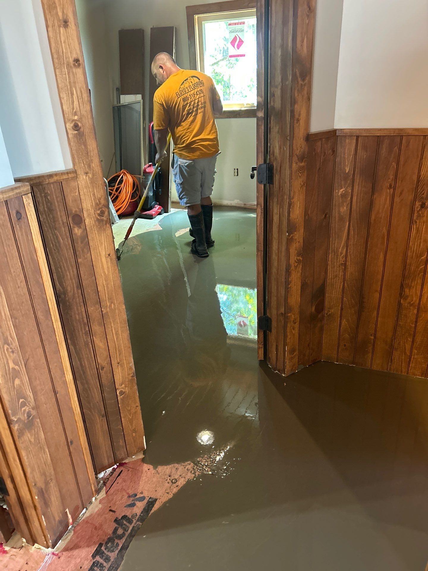 Flooded hallway with muddy water and a person in a yellow shirt standing near the door