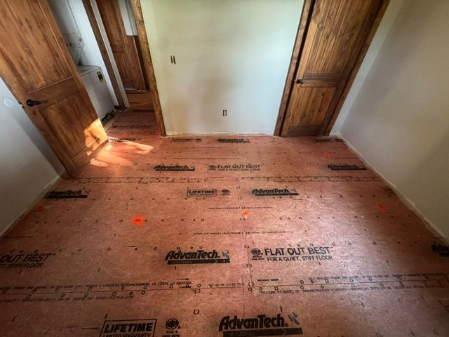 Small hallway with exposed subfloor, white walls, and two wooden doors.