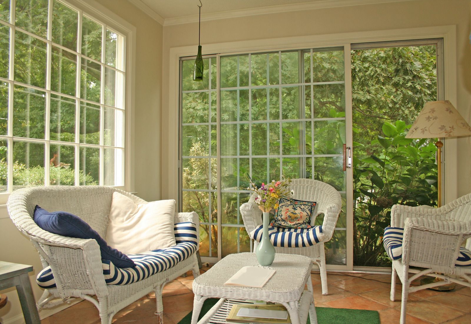 Bright sunroom with wicker chairs, blue-striped cushions, and large windows overlooking greenery