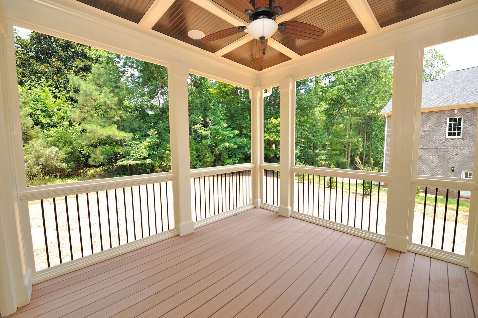 Covered wooden porch with white railings, ceiling fan, and trees beyond the open sides.
