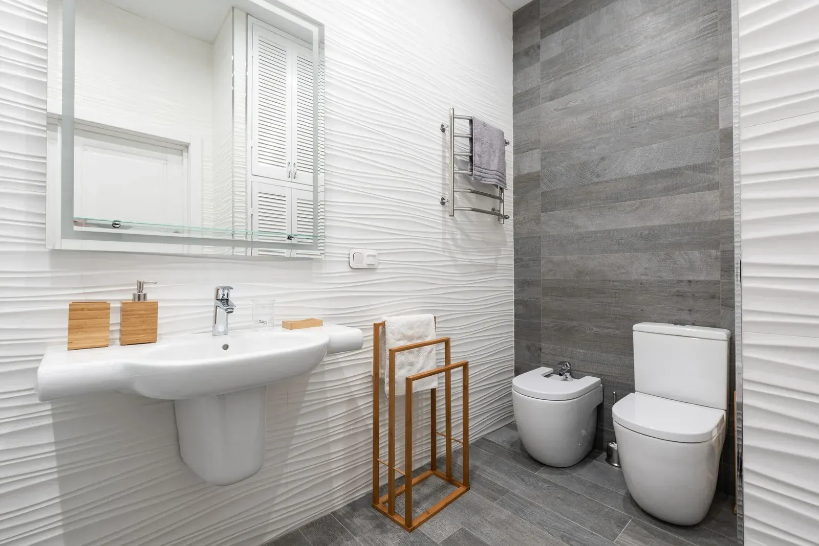 Modern white and gray bathroom with sink, mirror, bidet, toilet, and towel rack