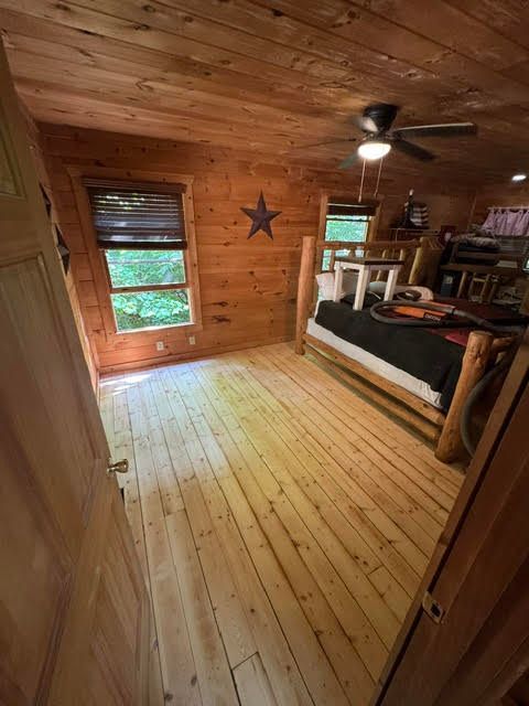 Wood-paneled cabin bedroom with wood floors, a bed, ceiling fan, and window overlooking greenery