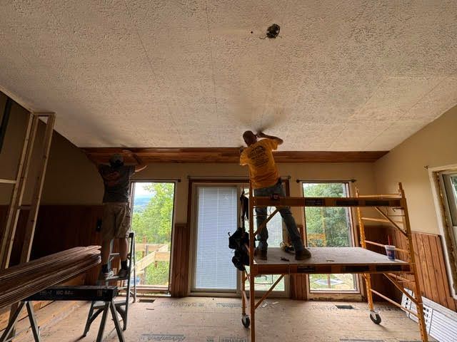 Worker on scaffolding installing a ceiling in a room with large windows and exposed walls
