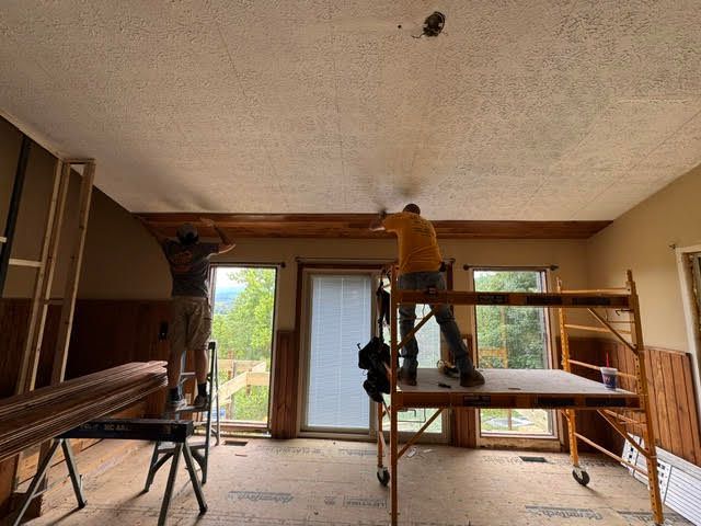 Person on scaffolding in a room under renovation, working near a large door and windows.