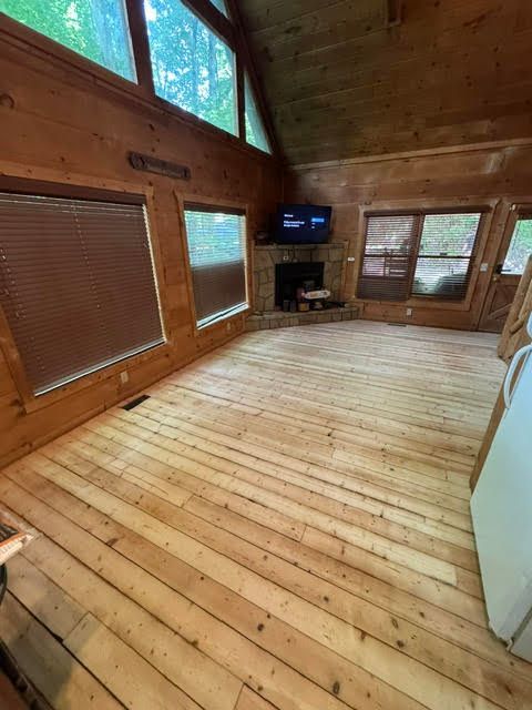 Empty wood-paneled room with vaulted ceiling, large windows, and a wall-mounted TV above a fireplace.