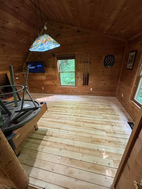 Wood-paneled cabin room with a skylight lamp, window, small screen, and bare wooden floorboards