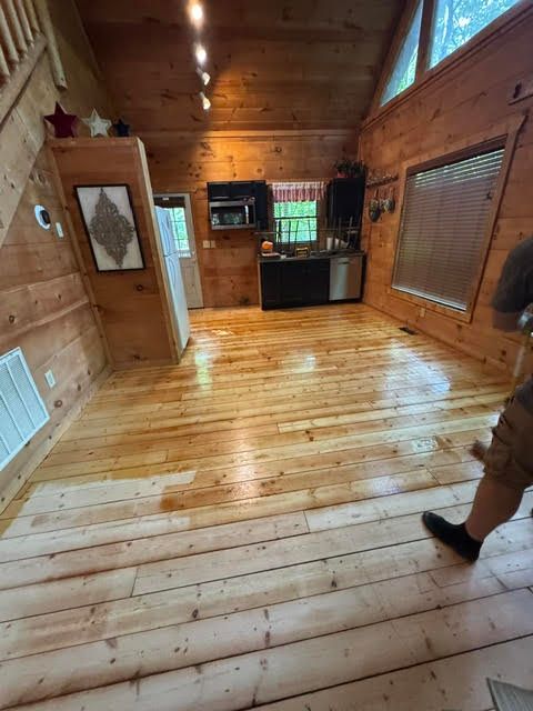 Wood-paneled cabin interior with polished wooden floors, windows, and a small kitchen area in back.
