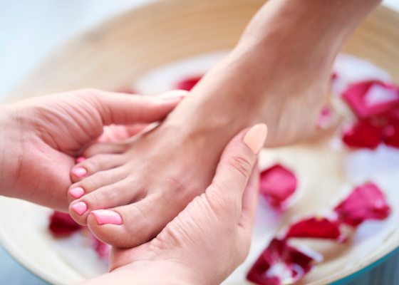 Uma mulher está fazendo uma massagem nos pés em uma tigela de água com pétalas de rosa.