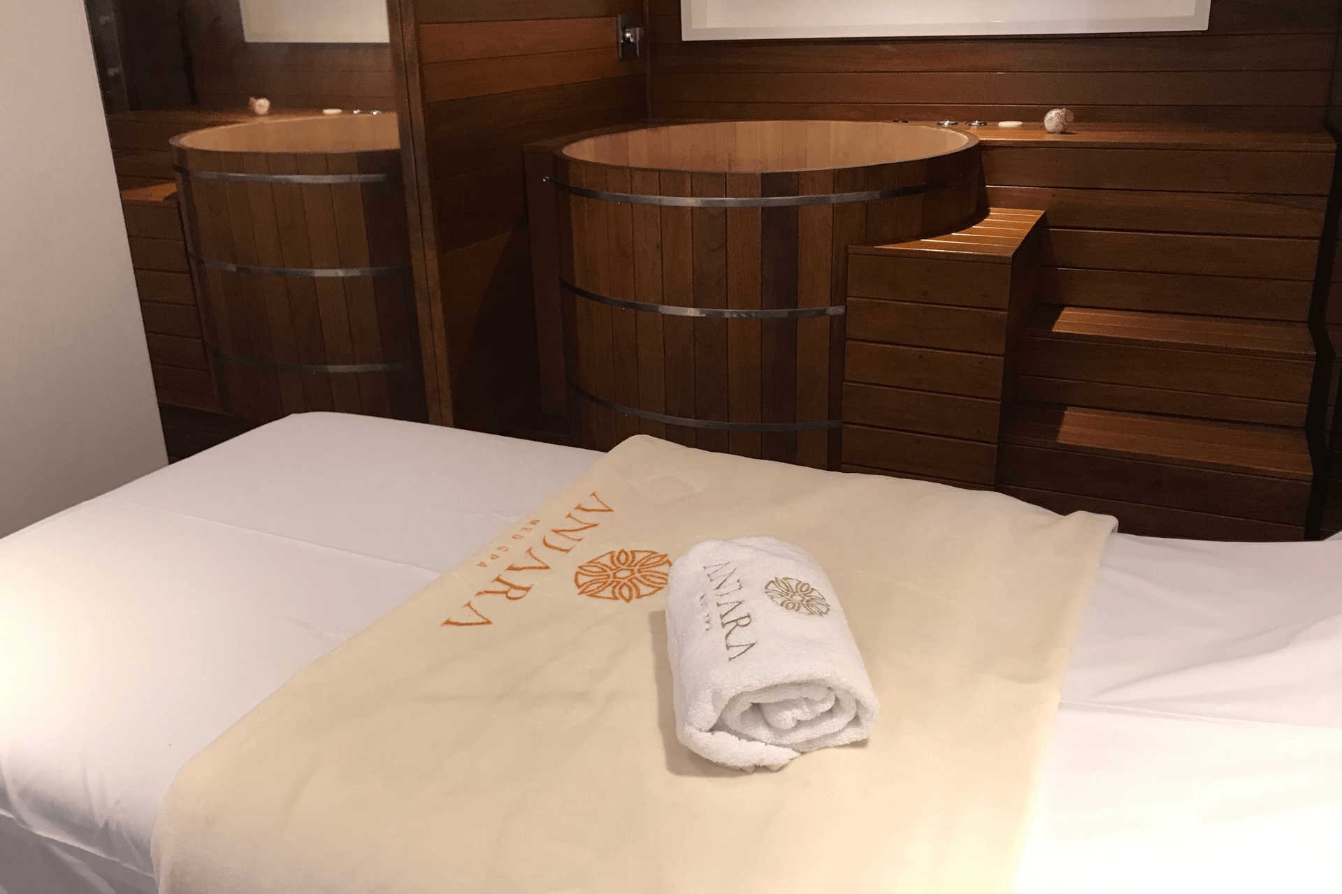 Uma cama com uma toalha e uma banheira de madeira ao fundo.