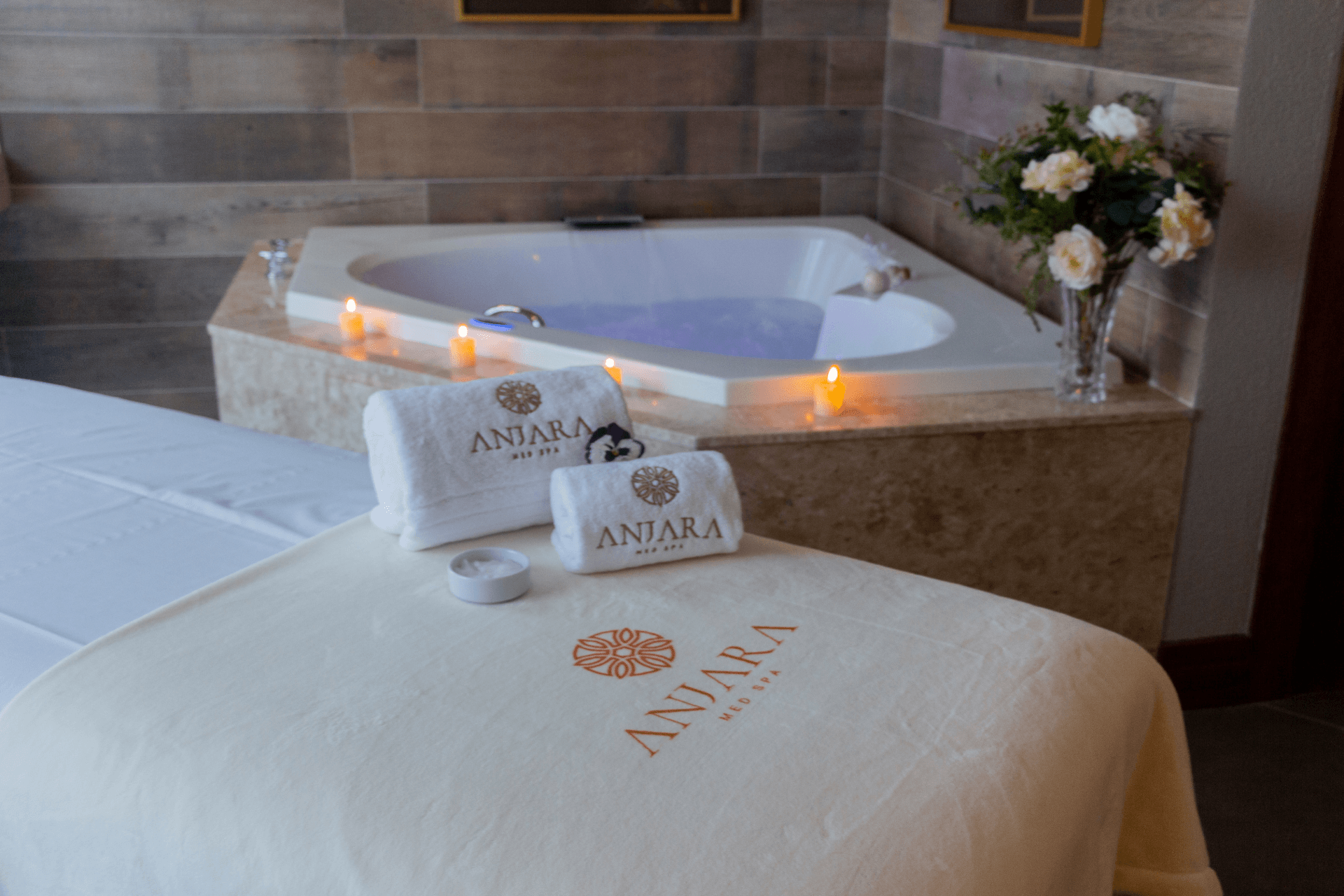 Uma mesa de massagem com toalhas e velas ao lado de uma banheira jacuzzi.