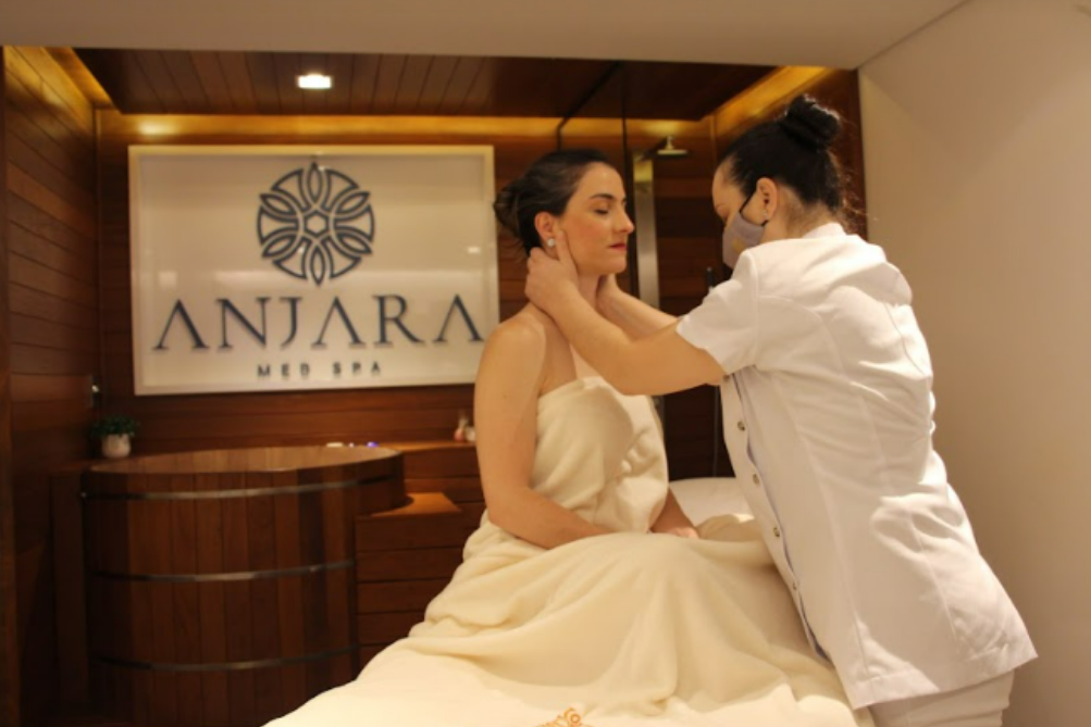 Uma mulher de vestido branco está recebendo uma massagem em frente a uma placa que diz anjara