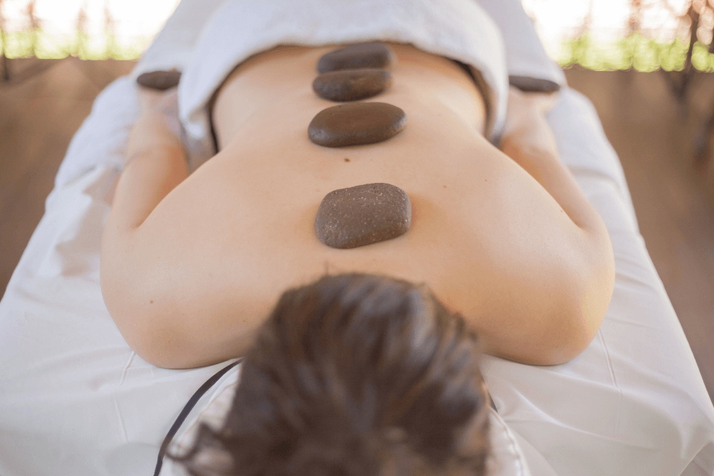 Uma mulher está deitada em uma mesa de massagem com pedras nas costas.