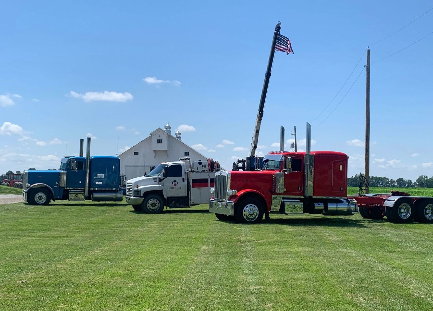 Three semi trucks are parked in a grassy field.