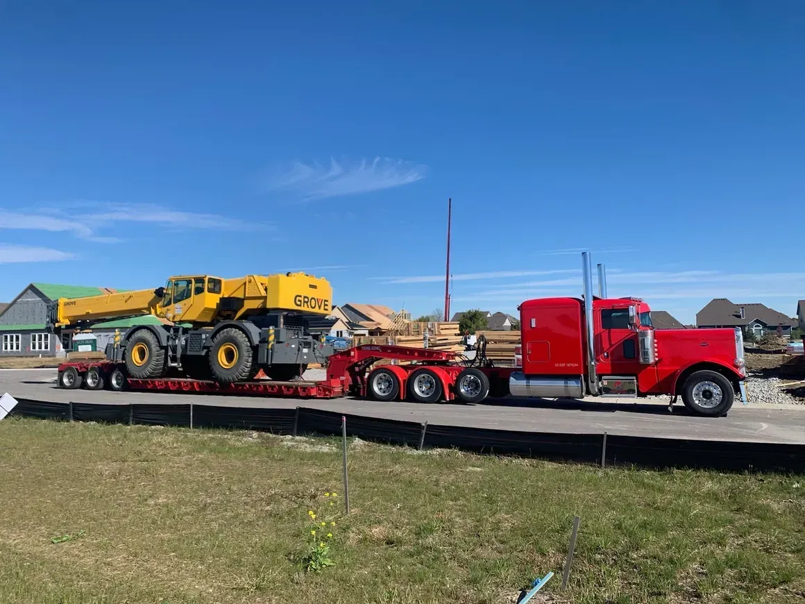 A red semi truck is carrying a yellow crane on a trailer.