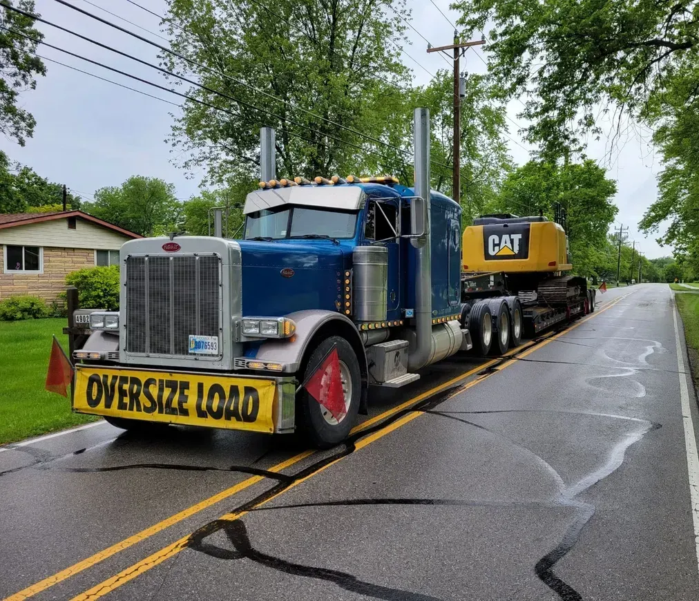A blue semi truck with a yellow bumper that says oversized load