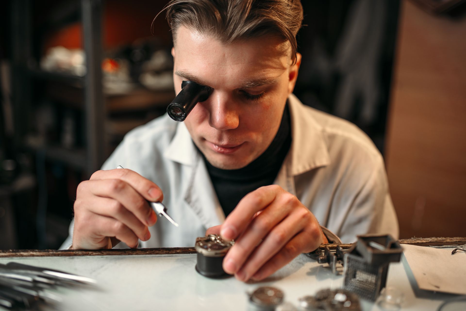 Technician using a magnifier to inspect a small part on a workbench.