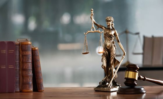 Lady Justice statue beside law books and a gavel on a wooden desk
