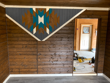 Wood-paneled room with a colorful geometric wall hanging above an open doorway to another room.